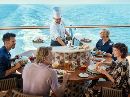 Vier Personen beim Essen auf einem Deck eines Mein Schiff Kreuzfahrtschiffs